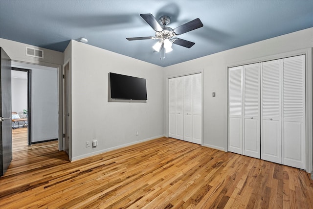 unfurnished bedroom with light wood-type flooring, ceiling fan, and two closets