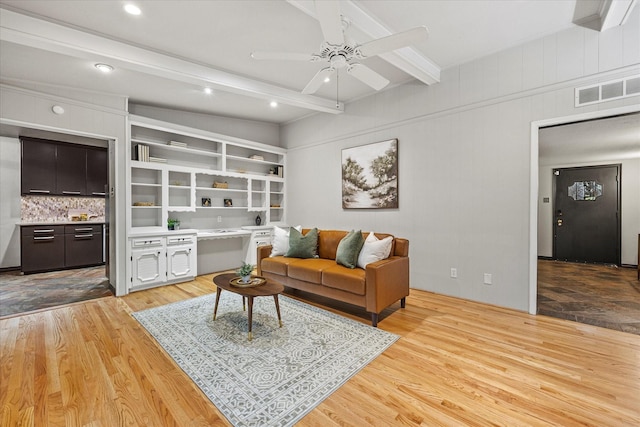 living room with ceiling fan, built in features, beam ceiling, and light hardwood / wood-style flooring