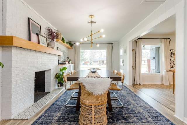 dining area with a brick fireplace, ornamental molding, light hardwood / wood-style floors, and a chandelier