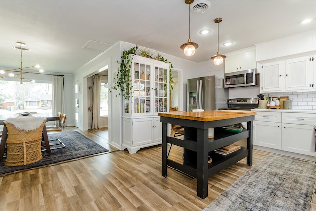 kitchen with stainless steel appliances, white cabinetry, and decorative light fixtures