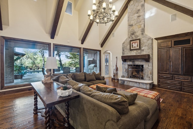 living room with a towering ceiling, beamed ceiling, a stone fireplace, an inviting chandelier, and dark hardwood / wood-style floors