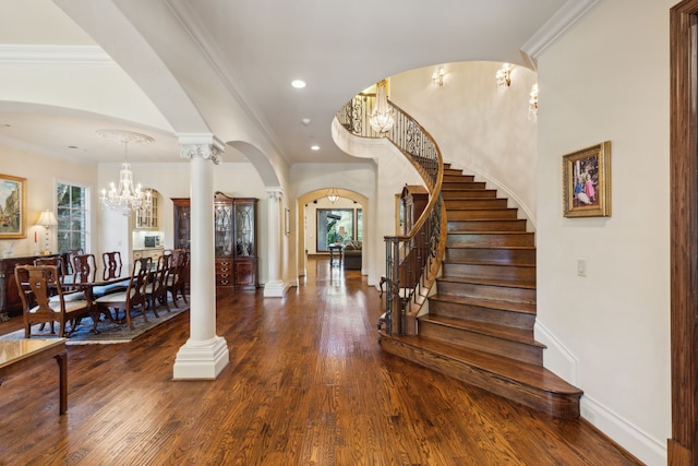 entryway featuring an inviting chandelier, dark hardwood / wood-style flooring, crown molding, and decorative columns