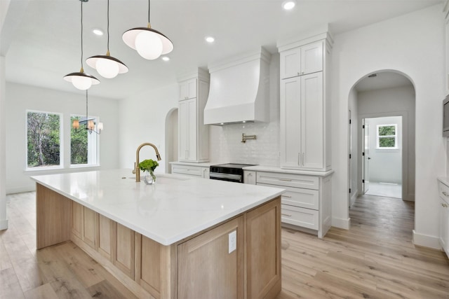 kitchen featuring a large island with sink, white cabinets, custom exhaust hood, electric stove, and sink