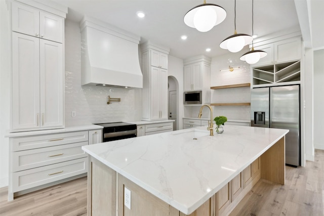 kitchen featuring a large island with sink, white cabinetry, stainless steel appliances, sink, and hanging light fixtures