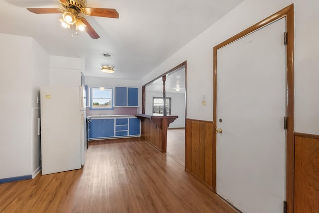 kitchen featuring ceiling fan, wood walls, white fridge, light wood-type flooring, and blue cabinetry