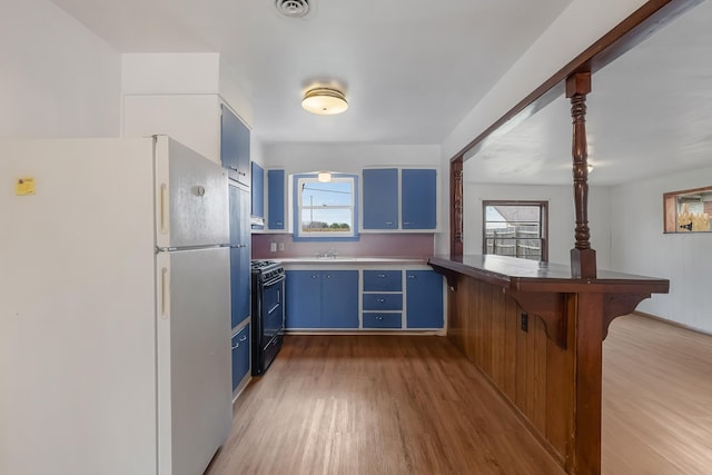 kitchen featuring white refrigerator, light hardwood / wood-style floors, blue cabinetry, black gas stove, and sink