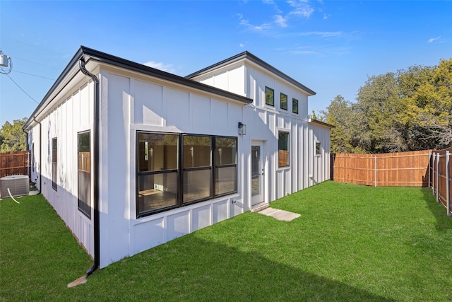 rear view of house featuring central AC unit and a lawn