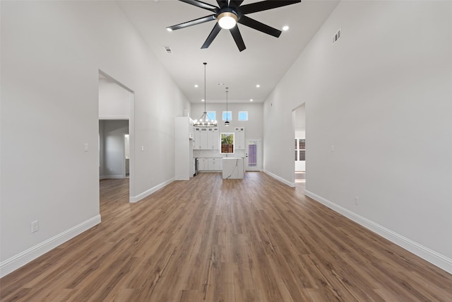 unfurnished living room featuring hardwood / wood-style flooring, ceiling fan with notable chandelier, and a high ceiling