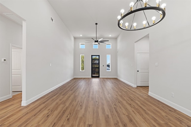 foyer entrance featuring ceiling fan with notable chandelier, light hardwood / wood-style floors, and a high ceiling