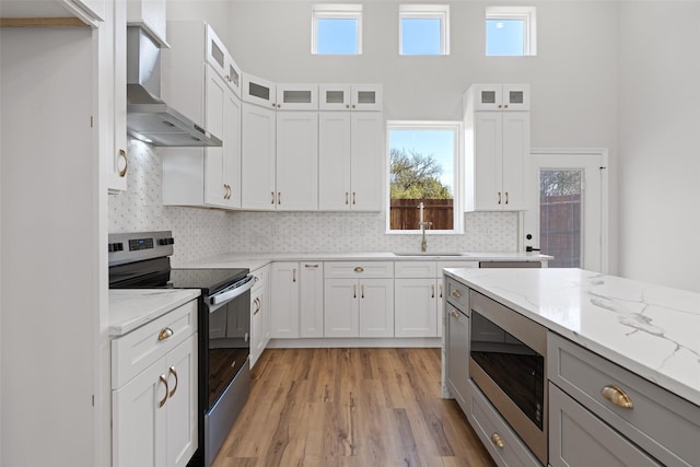 kitchen featuring electric stove, wall chimney range hood, white cabinets, and built in microwave