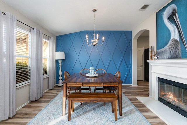 dining area with light wood-style flooring, a notable chandelier, an accent wall, visible vents, and a glass covered fireplace