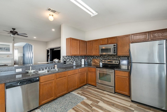 kitchen with appliances with stainless steel finishes, backsplash, light wood-type flooring, lofted ceiling, and sink