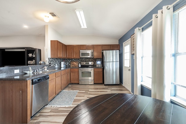 kitchen with tasteful backsplash, vaulted ceiling, light hardwood / wood-style floors, sink, and appliances with stainless steel finishes