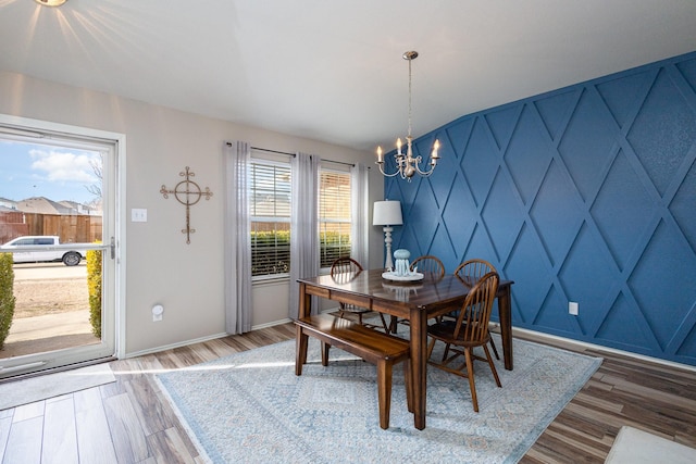 dining room with a notable chandelier, an accent wall, baseboards, and wood finished floors