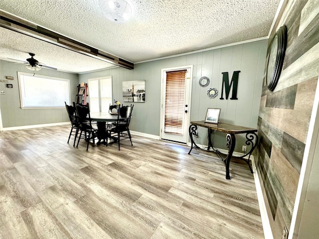 dining space featuring beam ceiling, a textured ceiling, wood-type flooring, wooden walls, and crown molding