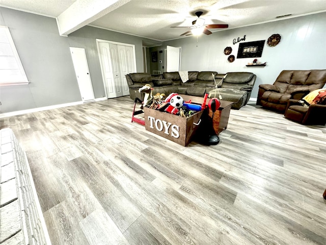 living room featuring a textured ceiling, light hardwood / wood-style floors, ornamental molding, ceiling fan, and beam ceiling