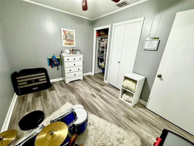 interior space with light hardwood / wood-style floors, wooden walls, ceiling fan, a textured ceiling, and crown molding