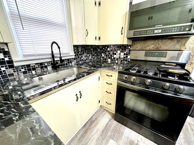 kitchen featuring backsplash, dark stone countertops, light hardwood / wood-style floors, sink, and stainless steel appliances