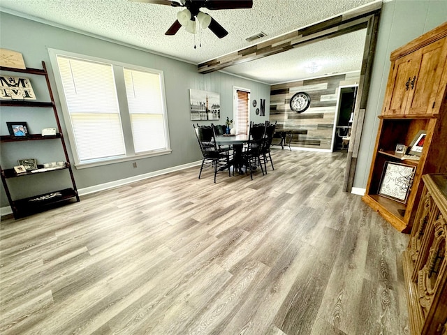 dining area featuring wood walls, ceiling fan, light wood-type flooring, a textured ceiling, and beamed ceiling