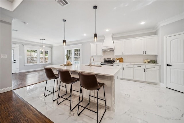 kitchen with premium range hood, white cabinetry, a kitchen island with sink, sink, and decorative light fixtures