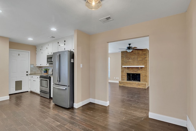 kitchen with a brick fireplace, stainless steel appliances, tasteful backsplash, dark wood-type flooring, and white cabinets