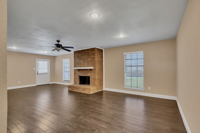 unfurnished living room featuring dark wood-type flooring, a fireplace, plenty of natural light, and ceiling fan