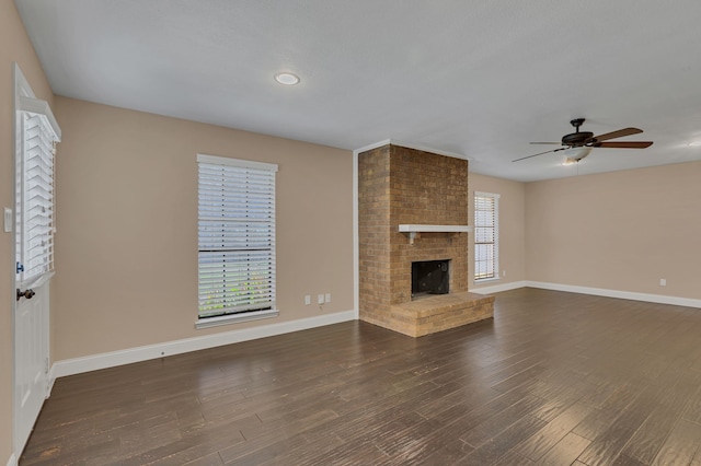 unfurnished living room featuring a brick fireplace, plenty of natural light, ceiling fan, and dark wood-type flooring