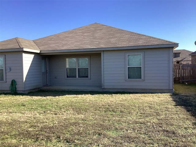 rear view of house featuring a shingled roof, fence, and a yard