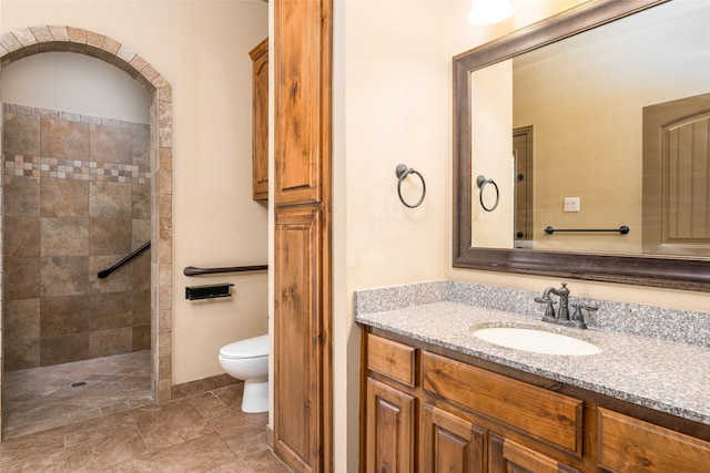 bathroom with toilet, tiled shower, and vanity