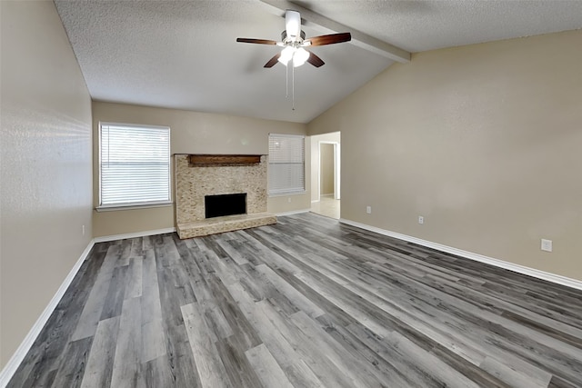 unfurnished living room with ceiling fan, a stone fireplace, hardwood / wood-style floors, a textured ceiling, and vaulted ceiling with beams