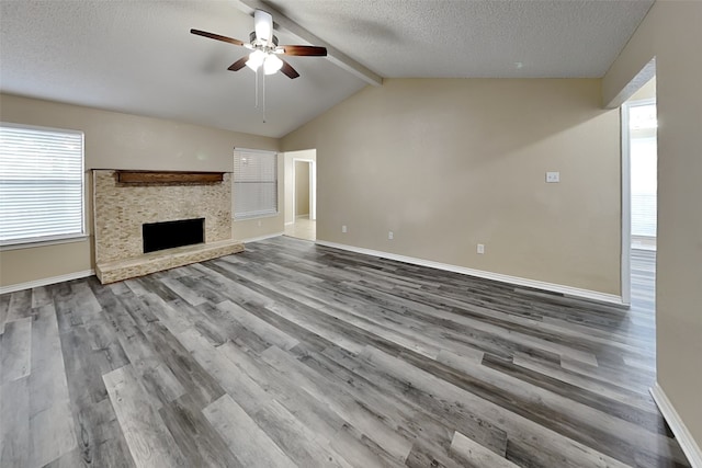 unfurnished living room with a textured ceiling, hardwood / wood-style floors, a fireplace, plenty of natural light, and lofted ceiling with beams