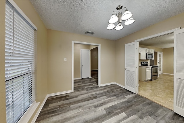 unfurnished dining area featuring light hardwood / wood-style floors, a textured ceiling, and a chandelier