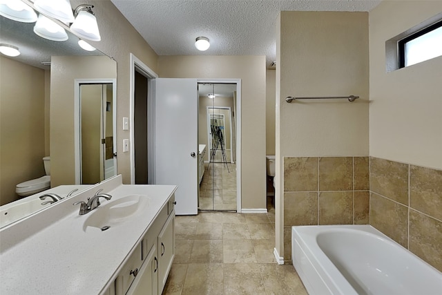 bathroom featuring a textured ceiling, toilet, a bath, and vanity