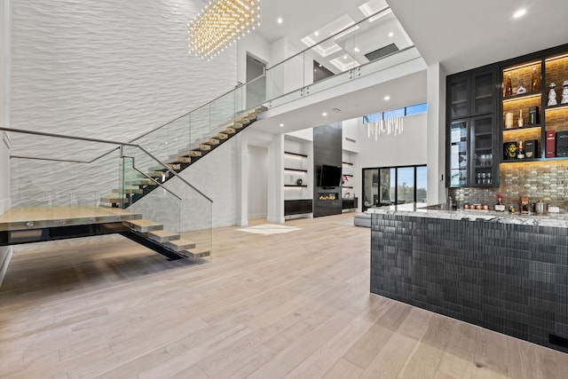 interior space featuring decorative backsplash, a high ceiling, light wood-type flooring, light stone countertops, and a chandelier