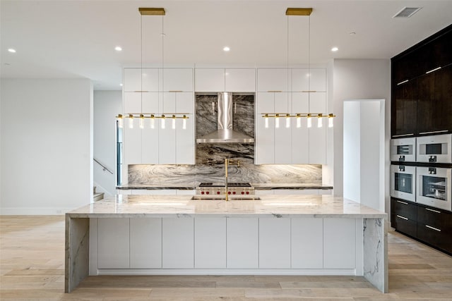 kitchen featuring white cabinets, a large island, wall chimney range hood, and pendant lighting