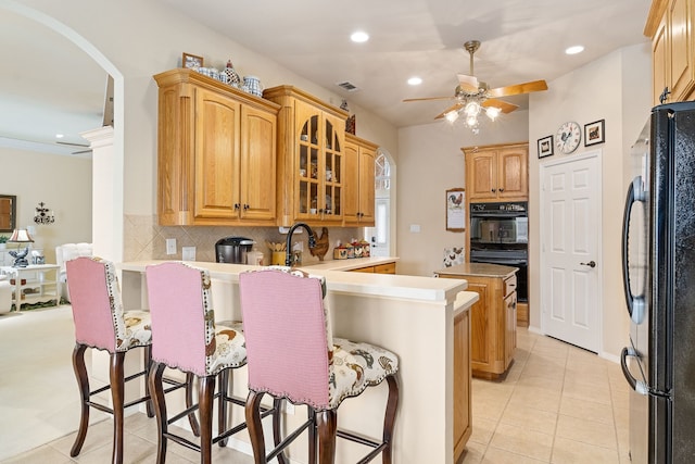 kitchen featuring black appliances, kitchen peninsula, a breakfast bar area, and tasteful backsplash