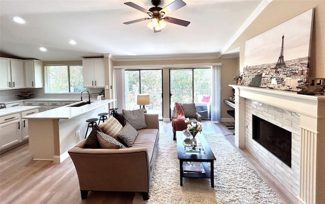 living room featuring vaulted ceiling, a brick fireplace, light hardwood / wood-style floors, sink, and crown molding