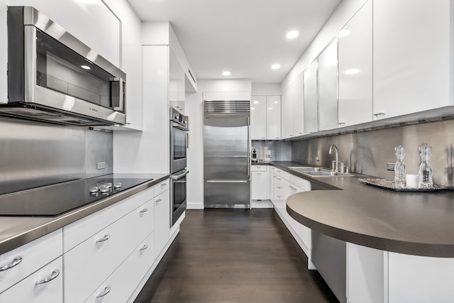 kitchen with appliances with stainless steel finishes, backsplash, dark wood-type flooring, white cabinets, and sink