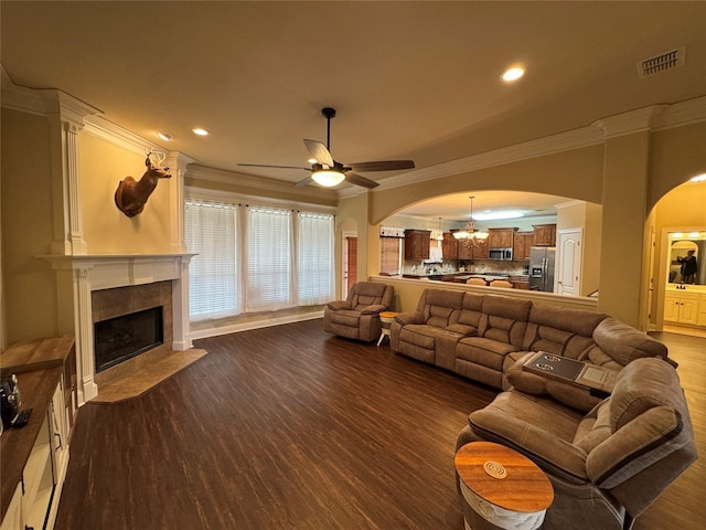 living area with arched walkways, dark wood-style flooring, crown molding, visible vents, and a tile fireplace