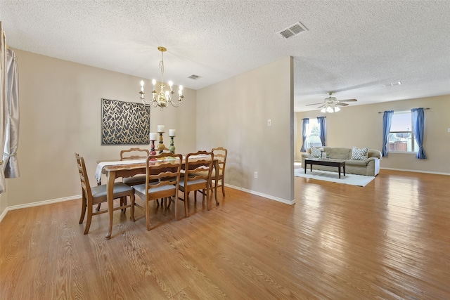 dining room with ceiling fan with notable chandelier, a textured ceiling, and light wood-type flooring