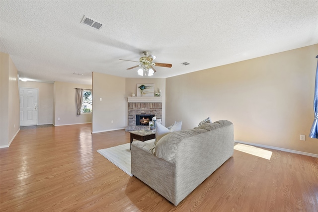 living room featuring a brick fireplace, light hardwood / wood-style floors, a textured ceiling, and ceiling fan