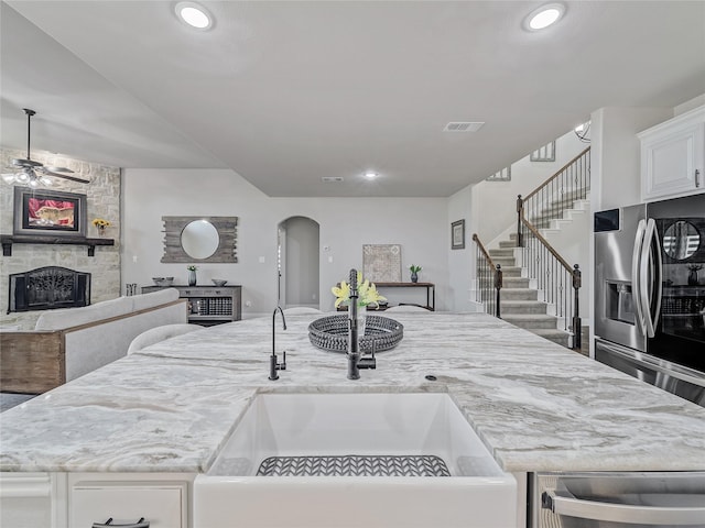 kitchen featuring sink, white cabinetry, light stone countertops, a stone fireplace, and stainless steel fridge