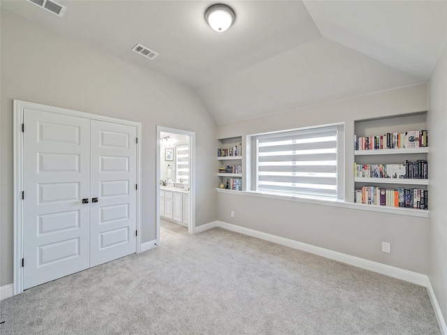 unfurnished bedroom featuring light carpet, a closet, ensuite bathroom, and lofted ceiling