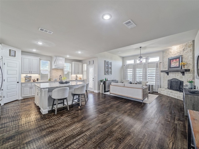 kitchen featuring white cabinetry, a kitchen bar, a stone fireplace, dark wood-type flooring, and a kitchen island