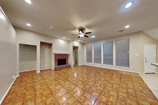 unfurnished living room with a textured ceiling, a brick fireplace, light parquet floors, and ceiling fan