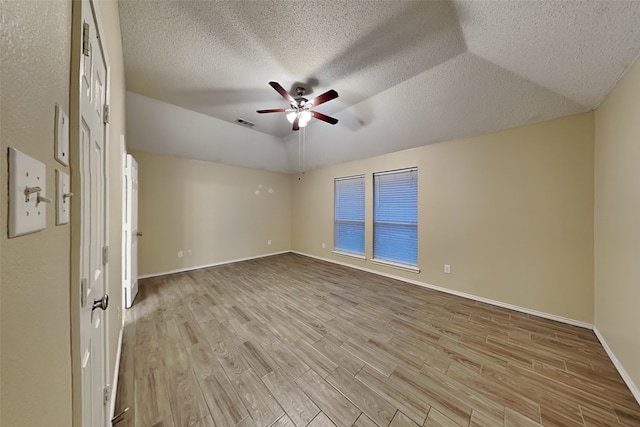 spare room with ceiling fan, vaulted ceiling, a tray ceiling, and light hardwood / wood-style floors