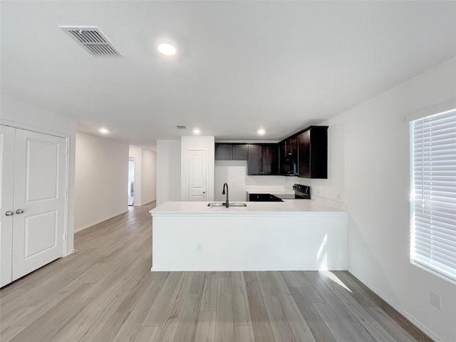 kitchen with light hardwood / wood-style floors, kitchen peninsula, sink, plenty of natural light, and black / electric stove