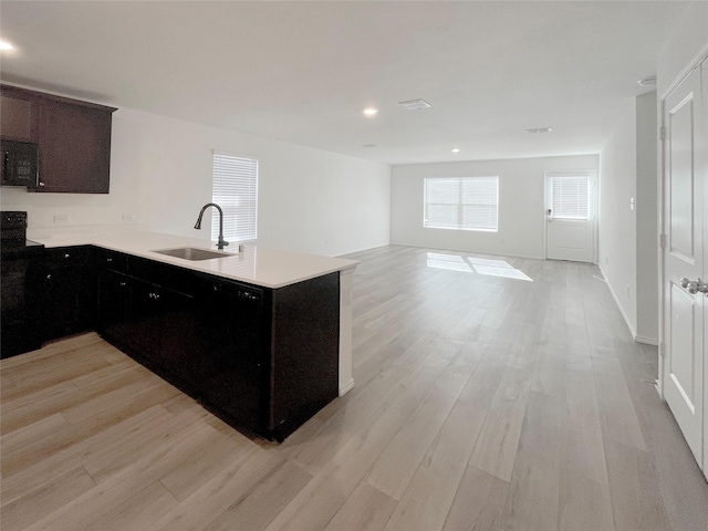 kitchen featuring light hardwood / wood-style floors, stove, kitchen peninsula, sink, and black dishwasher