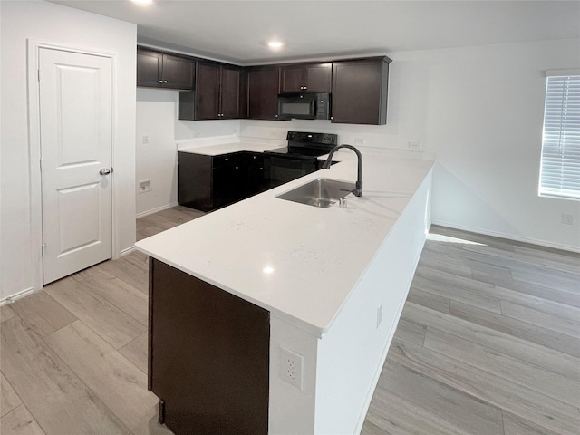 kitchen with sink, black appliances, kitchen peninsula, and light wood-type flooring