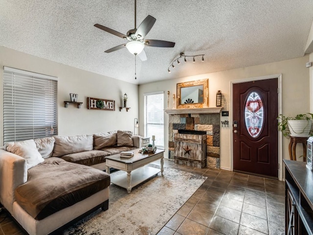 living room featuring ceiling fan, a stone fireplace, and a textured ceiling